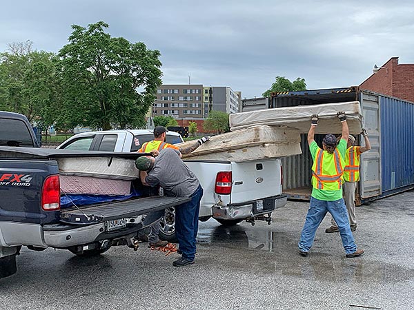 four men unloading old mattresses from two pickup trucks